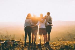 Four family members standing together with arms around each other, looking out at a scenic sunset, symbolizing support, unity, and hope in recovery.