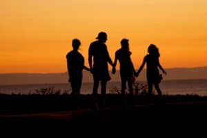 A silhouette of a family is shown holding hands as they support their teen boy who is in addiction recovery.