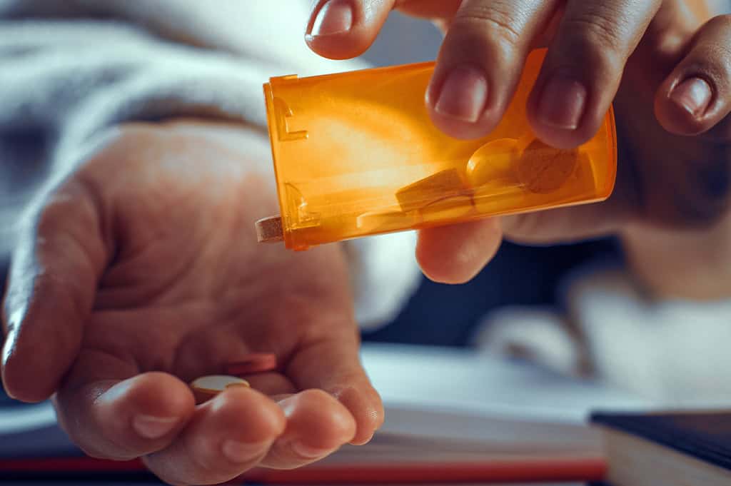 person dumping out pills into their hand from a pill bottle