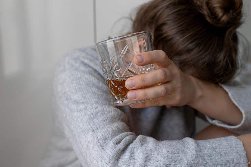 woman holding a glass of dark liquor showing signs of alcohol dependency