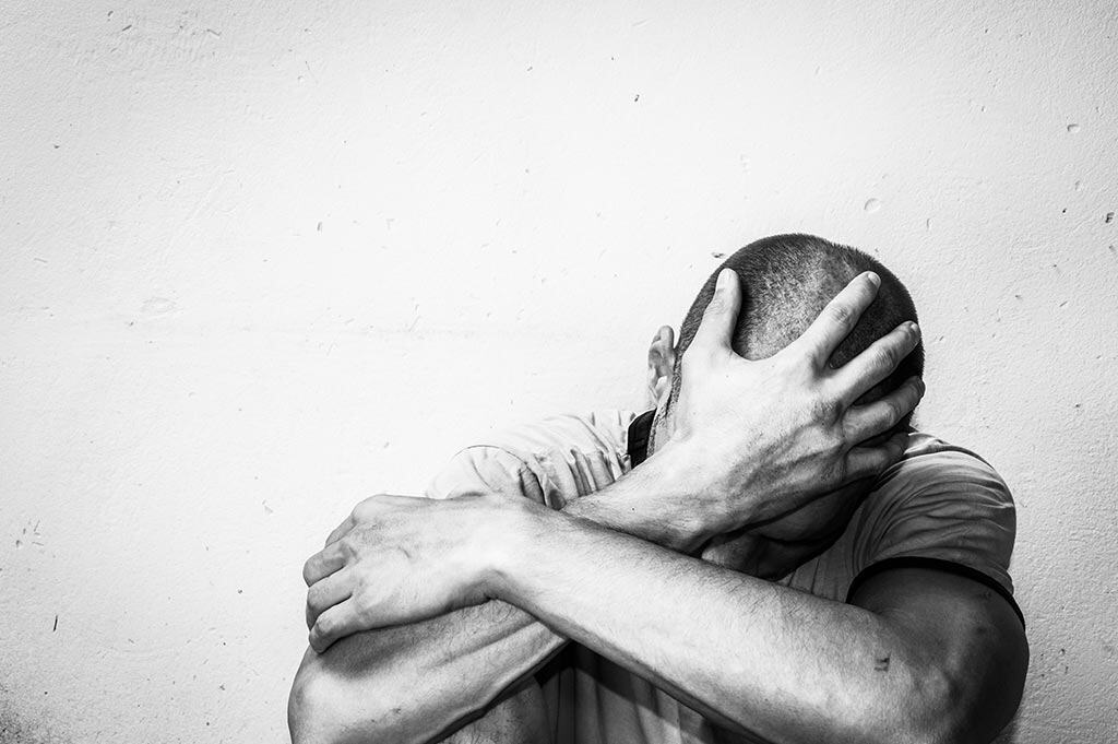 Distraught man holding his head showing signs of hitting rock bottom with addiction