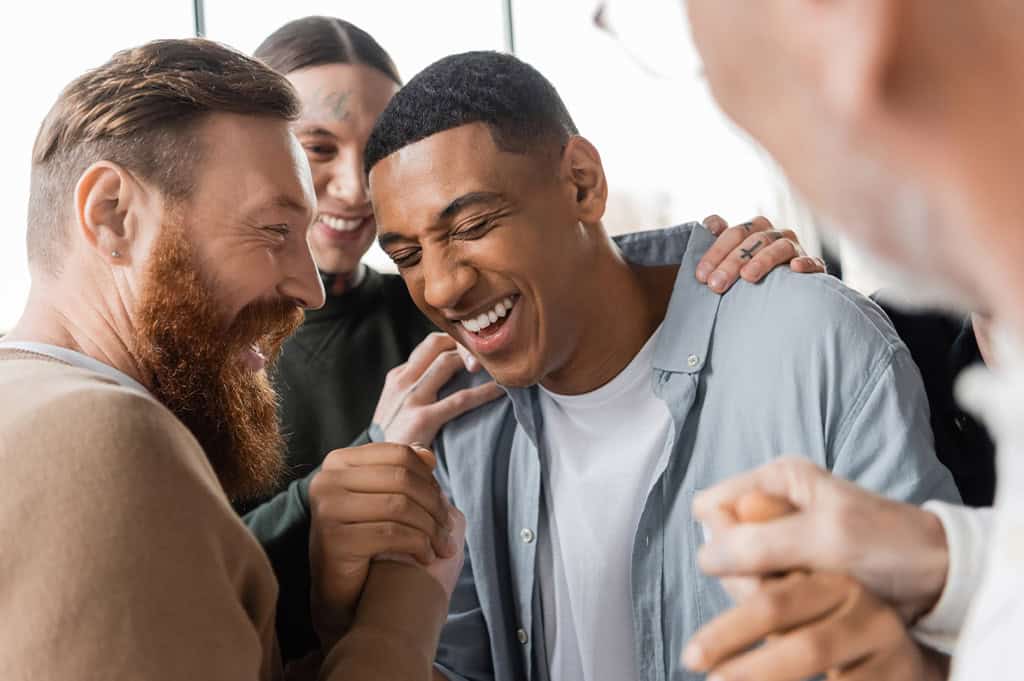 four men gathered around each other laughing during men's addiction treatment
