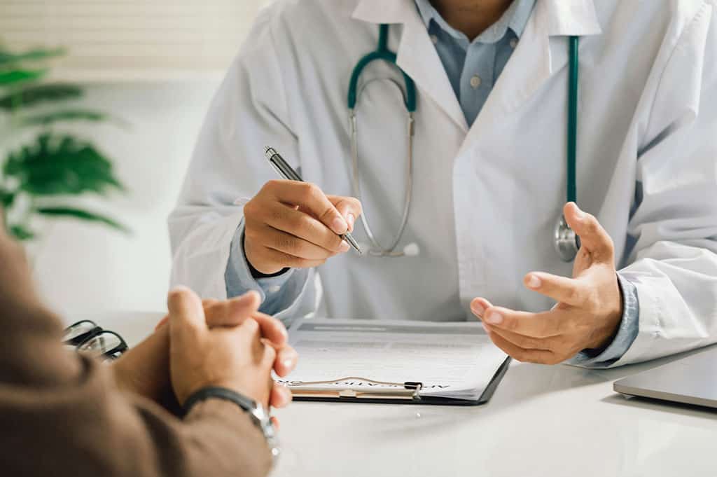 A clinician in a white coat discusses treatment options with a patient during a medical consultation.