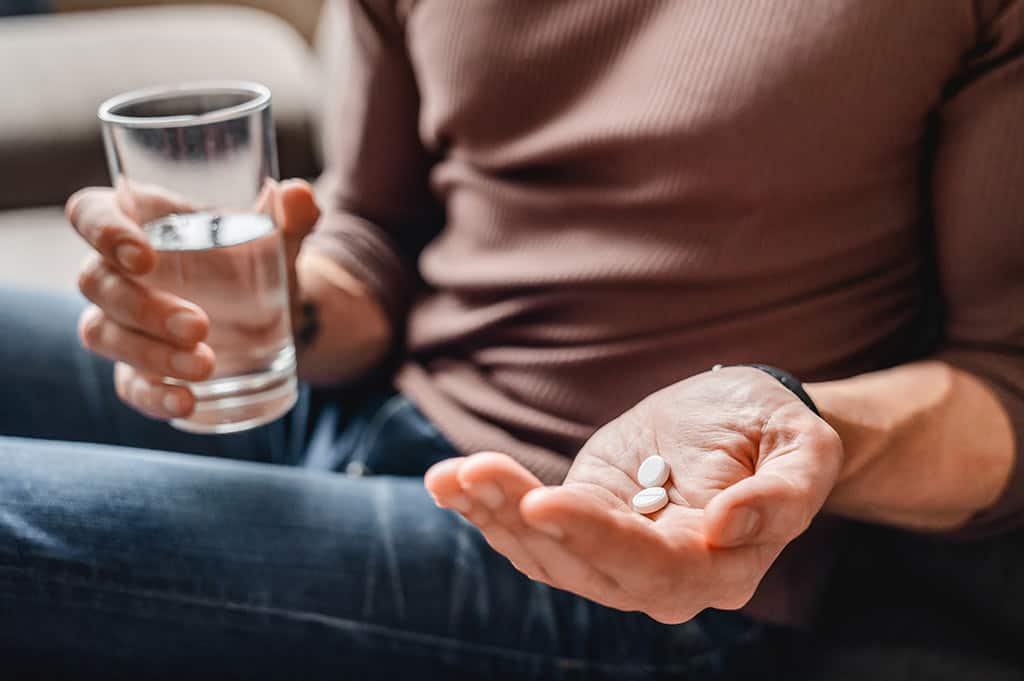 man in a brown shirt and jeans holding two white suboxone pills with a glass of water
