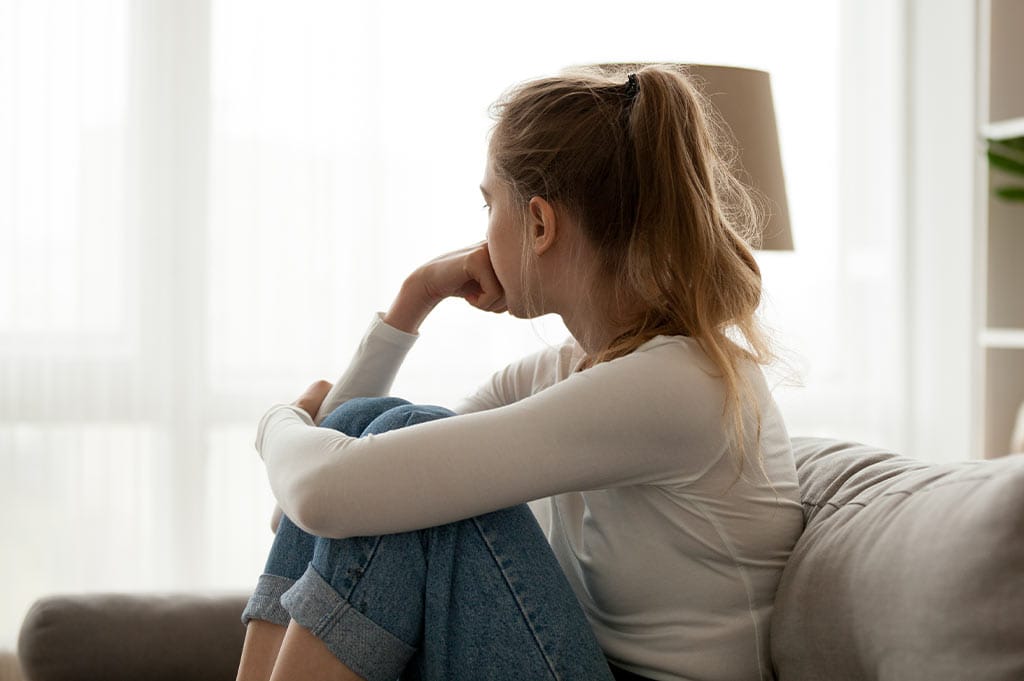 A young woman sits on her couch, deep in thought about whether Suboxone is addictive.