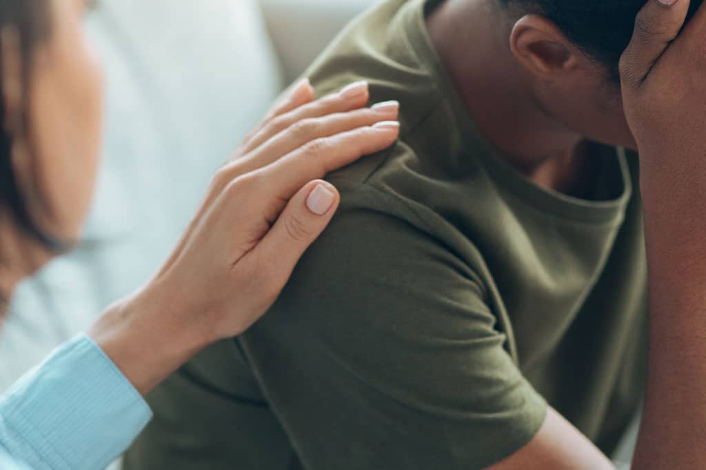 Woman rests a hand on the shoulder of a man sitting with his head in his hand during a difficult conversation
